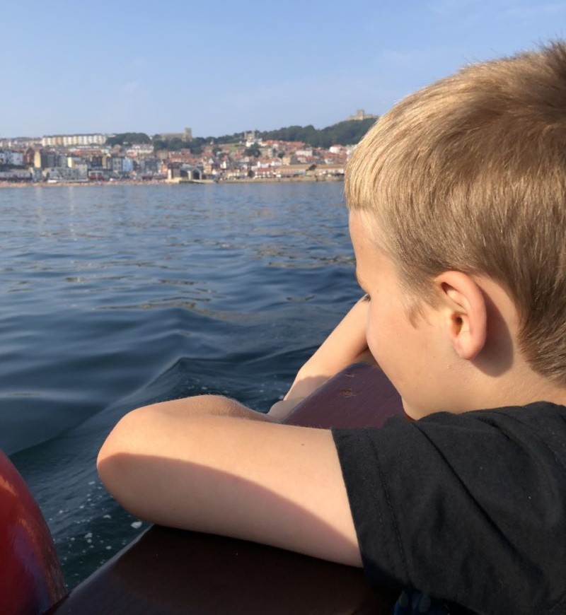 A boy leaning on the edge of a boat looking out to sea.