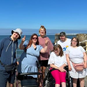 Group Holidays Men and women having a group photo taken on a sea wall path in front of the sea.