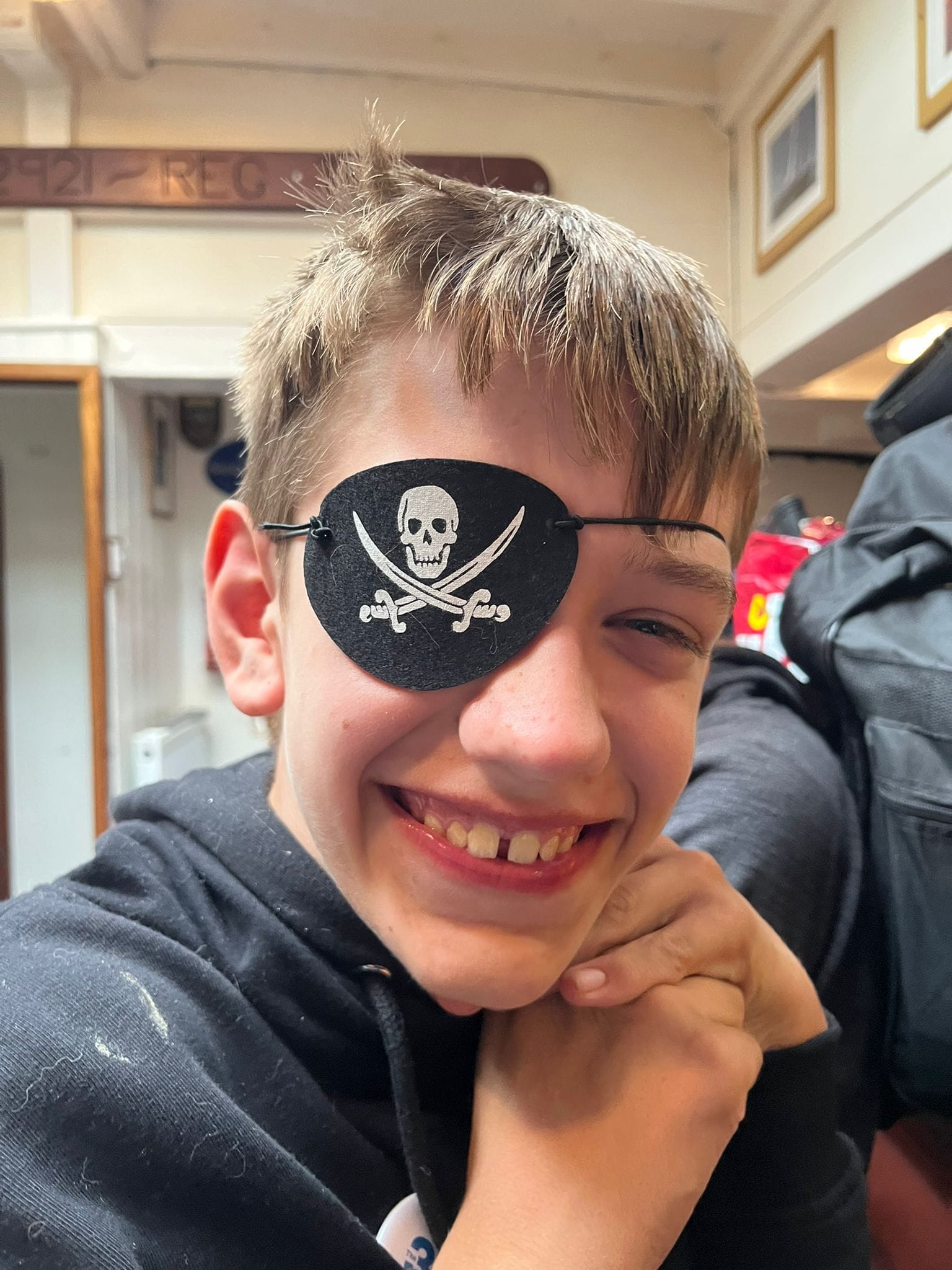 A boy smiling at the camera with a pirate eye patch on.