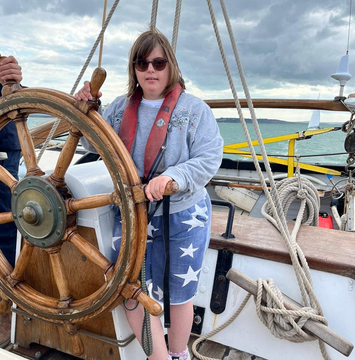 Young person steering the boat using the large wooden wheel.