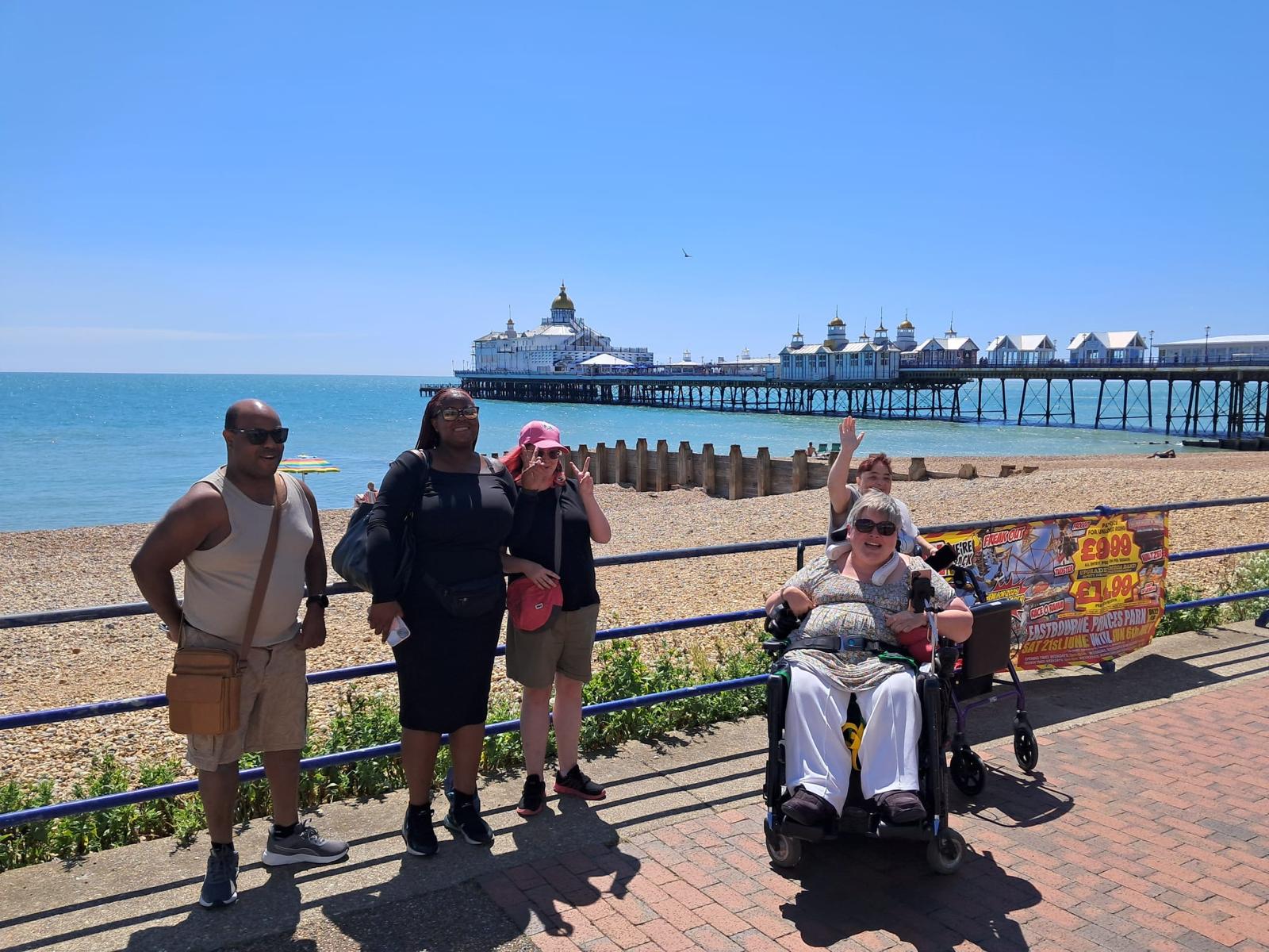 A group of men and women standing on a promenade with the sea and Eastbourne pier behind them.