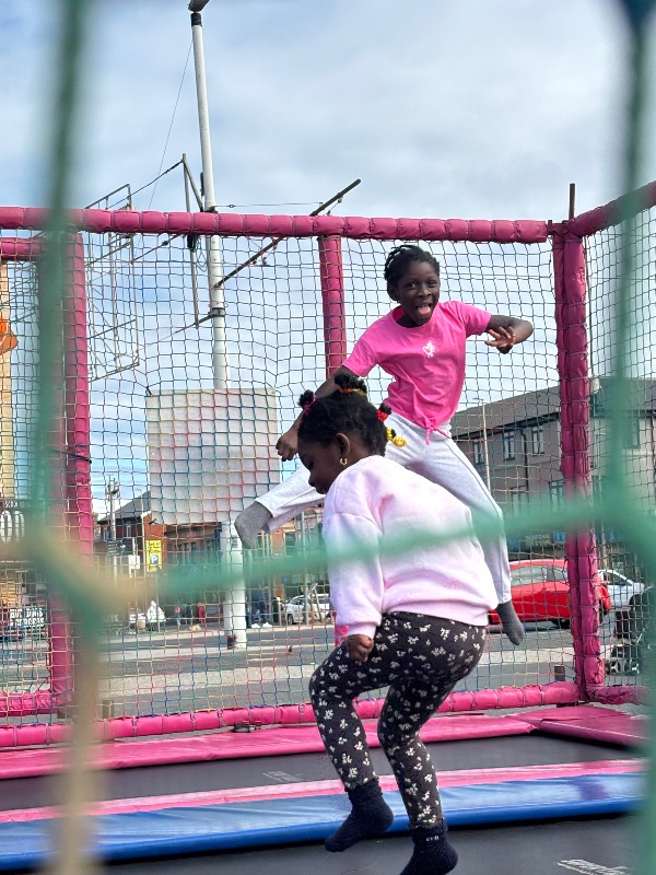 Two girls jumping on a trampoline, both wearing pink tops.