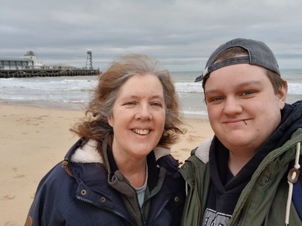 A lady and teenage boy smiling at the camera on a windy beach. 