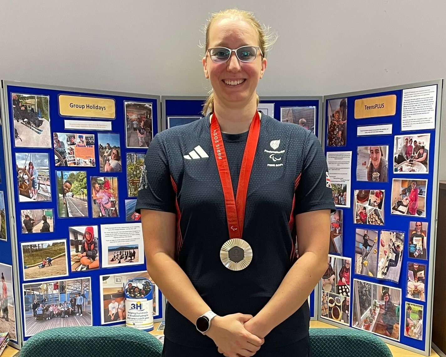 Callie-Ann Warrington stands in front of blue boards with photos of beneficiaries enjoying there breaks away.