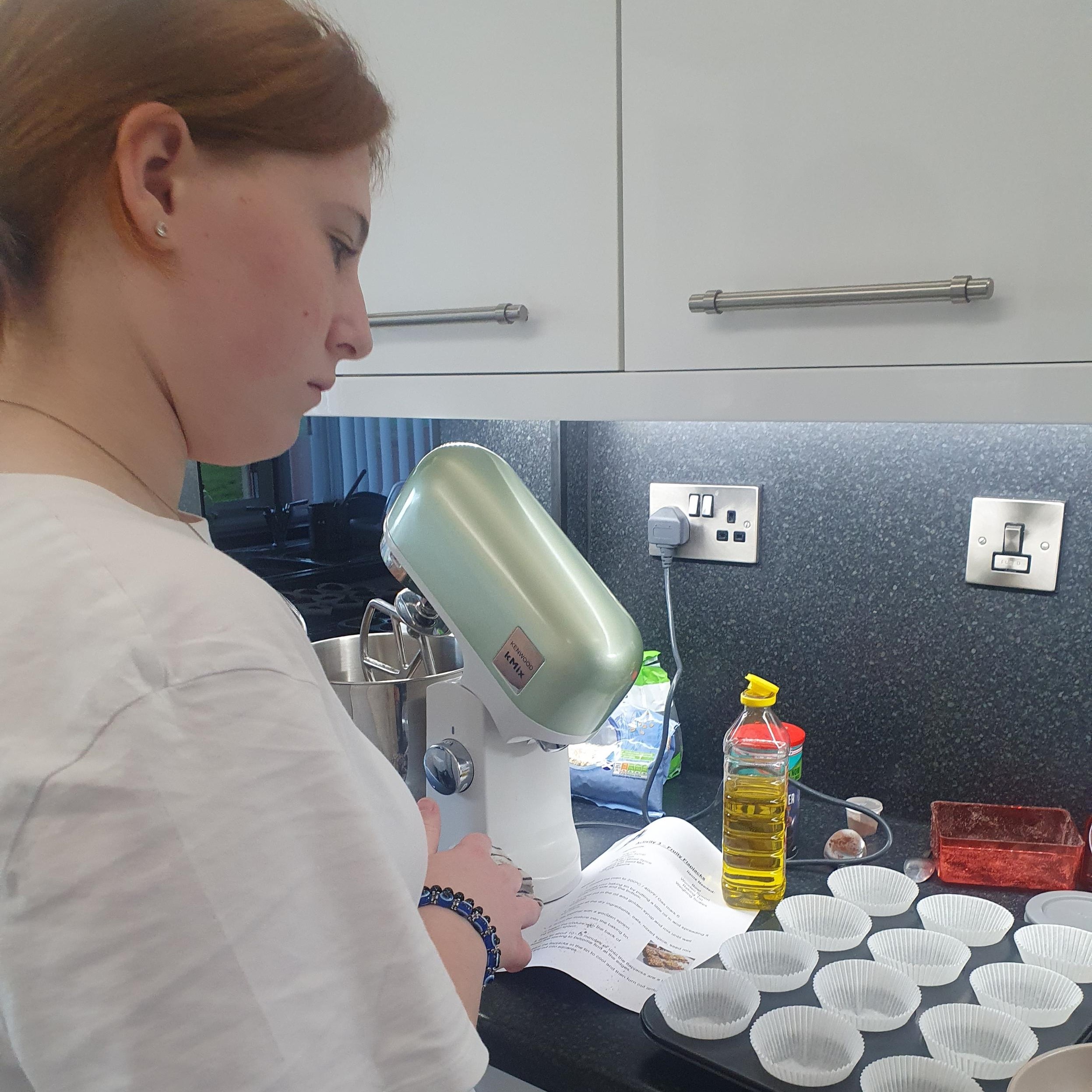 A young lady facing away from the camera, reading the instructions for a baking activity.