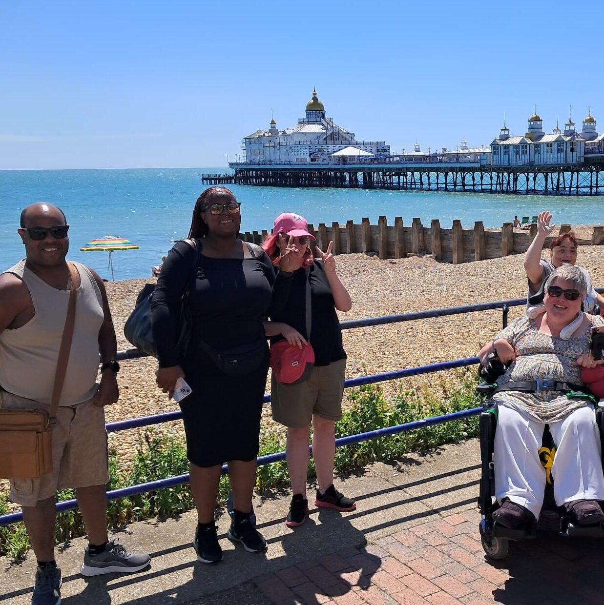 A group of people standing with the sea and pier behind them smiling at the camera.