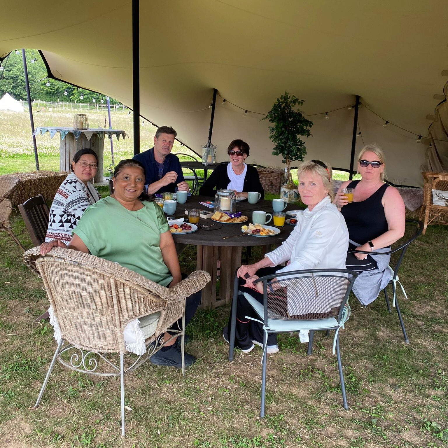 A group of people sitting at a table under a canvas tent smiling at the camera.
