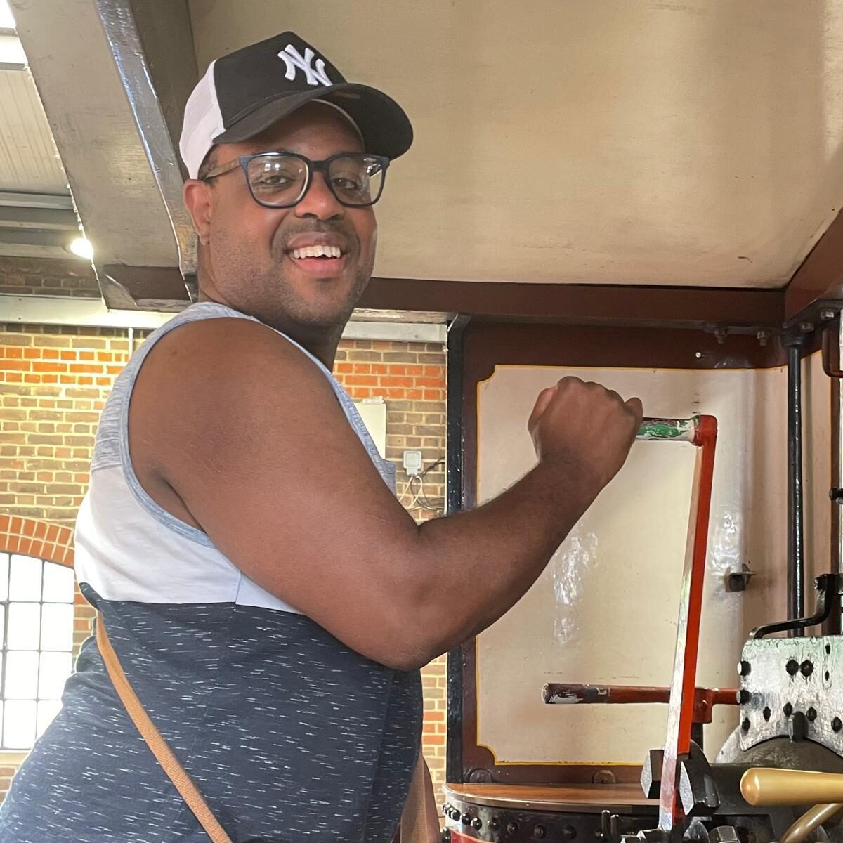 A man wearing a baseball cap turning a handle on part of a train.