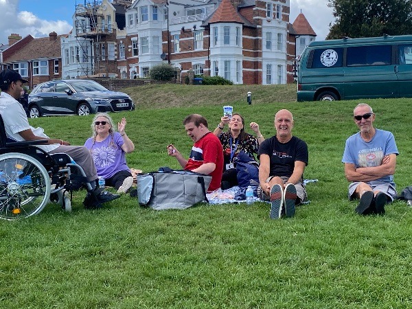 A group of holiday guests sitting on a lawn in front of a large old building.